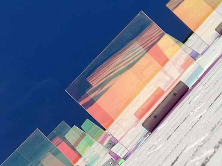 Mehrere transparente, farbige Glasplatten in unterschiedlicher Höhe auf einer weißen Treppe vor blauem Himmel