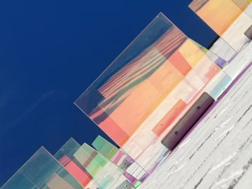Mehrere transparente, farbige Glasplatten in unterschiedlicher Höhe auf einer weißen Treppe vor blauem Himmel