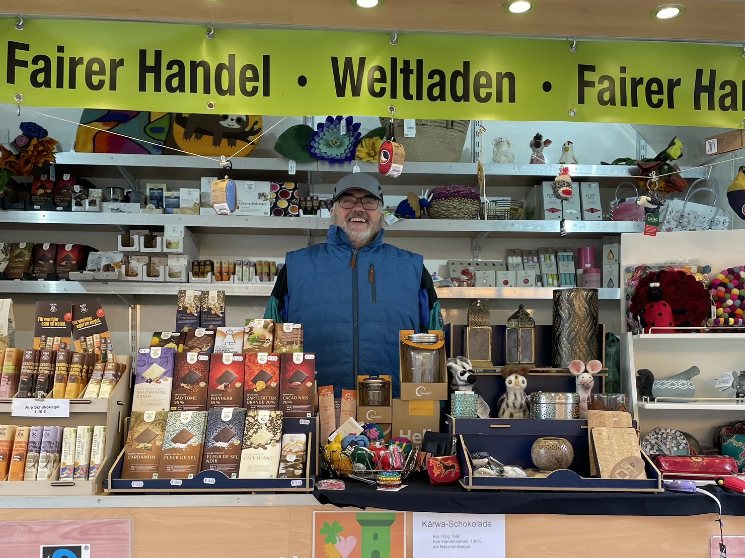 Fairtrade-Stand mit Leckereien und lachendem Verkäufer. Klick öffnet Bild in größerer Ansicht.