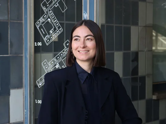 Melina Hüttner mit schwarzem Sakko vor einer Glaswand mit weißer Gebäudegrundrisszeichnung Klick öffnet die Meldung.