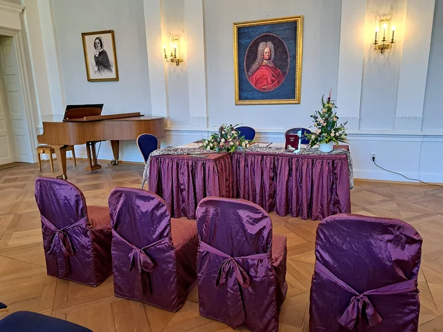 Festsaal ist mit Blumenschmuck und Sesseln für Trauung vorbereitet. Klick öffnet die Meldung.