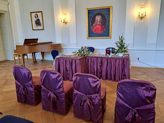 Festsaal ist mit Blumenschmuck und Sesseln für Trauung vorbereitet. Klick öffnet die Meldung.