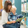 Junge Mutter liest ihrem Kind vor den Bücherregalen eine Bücherei vor. 