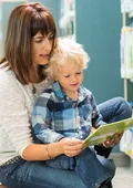 Junge Mutter liest ihrem Kind vor den Bücherregalen eine Bücherei vor. 