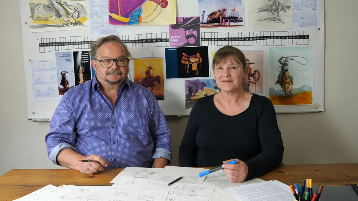 Illustratorin Petra Herberger und Autor Jochen Findeiss vor ihrem Moodboard mit Studien und Zeichnungen zur Graphic Novel "Horse Man Jean-Claude Dysli. Ein schweizer Cowboy in den USA"