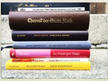 Bücherstapel mit Titeln von Fürther Autoren, darunter Werke von Jakob Wassermann, Ewald Arenz, Evi Kurz und Beatrix Müller-Kampel.