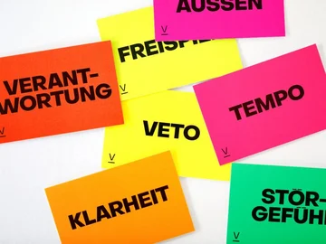 Mehrere bunte Karten mit großen schwarzen Druckbuchstaben liegen verstreut auf weißem Untergrund