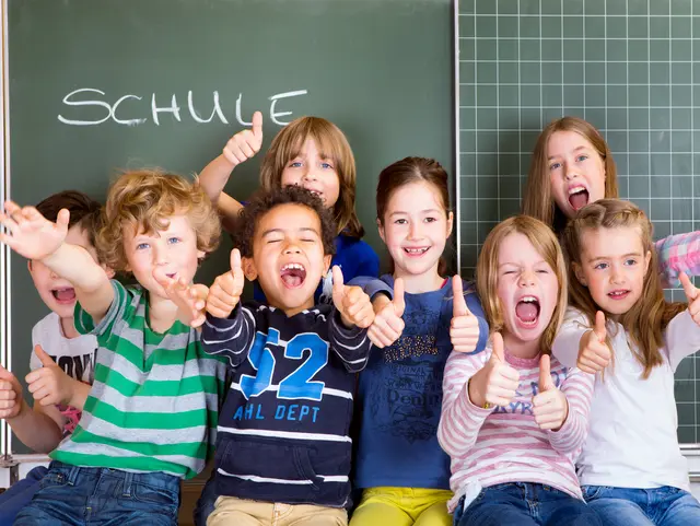 Eine Gruppe ausgelassener Schulkinder vor einer Schultafel.