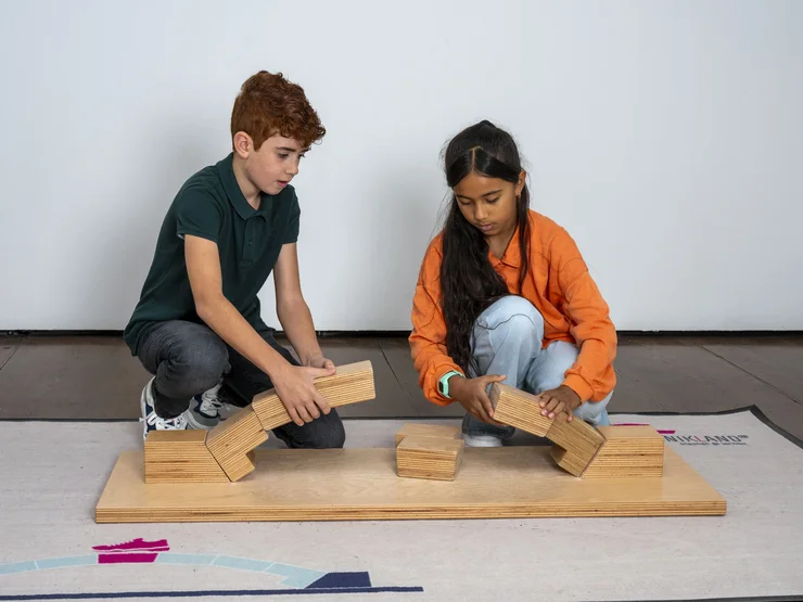 Ein Mädchen und ein Junge bauen gemeinsam eine Brücke aus Holzspielzeug. Klick öffnet Veranstaltungstipp.