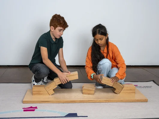 Ein Mädchen und ein Junge bauen gemeinsam eine Brücke aus Holzspielzeug. Klick öffnet Veranstaltungstipp. 