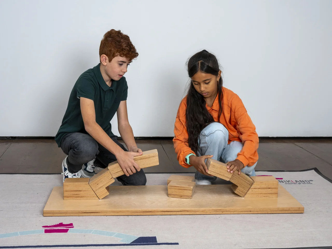 Ein Mädchen und ein Junge bauen gemeinsam eine Brücke aus Holzspielzeug.