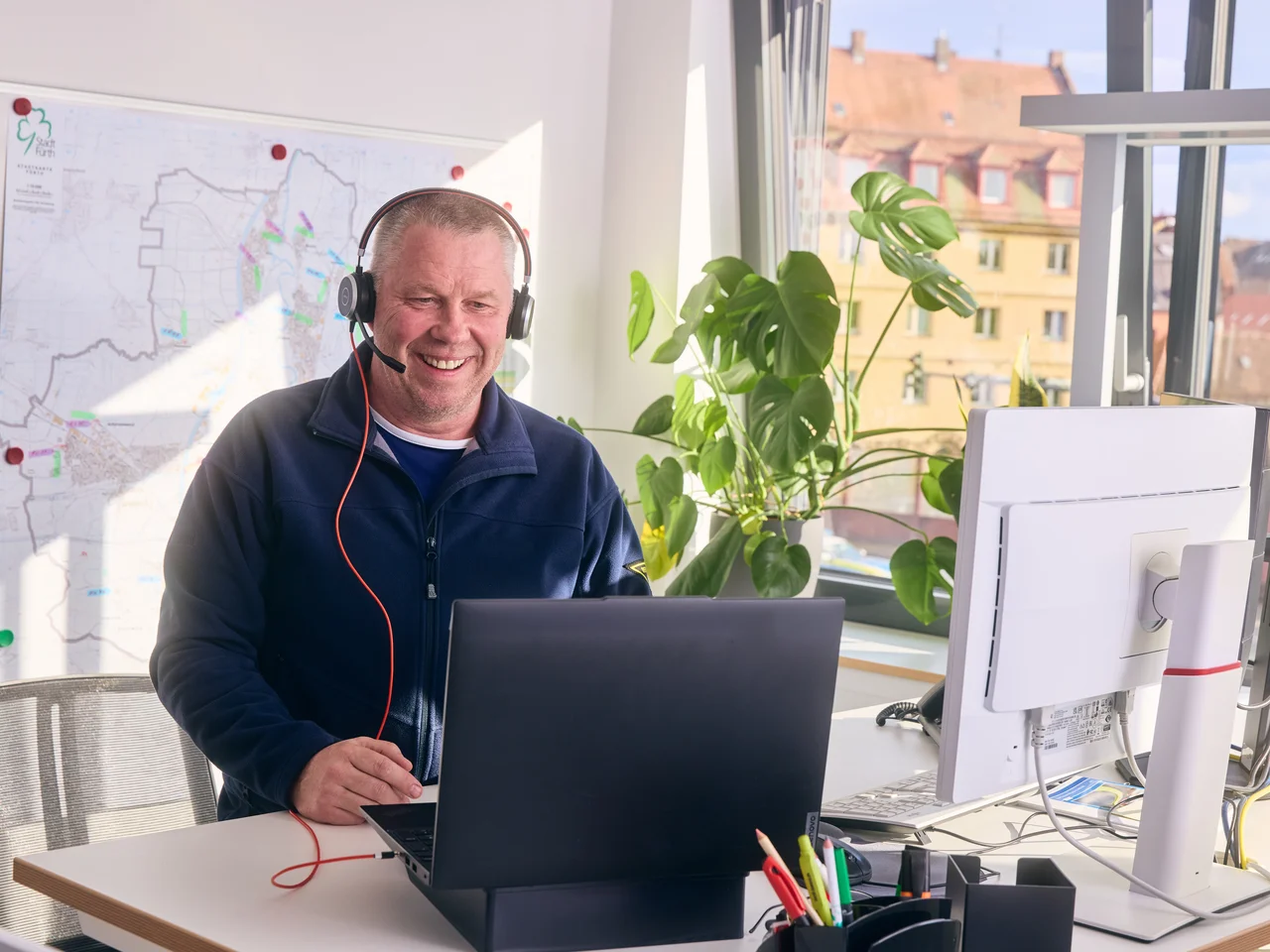 Mann mit Headset steht am Schreibtisch mit Laptop und Monitor im Büro.