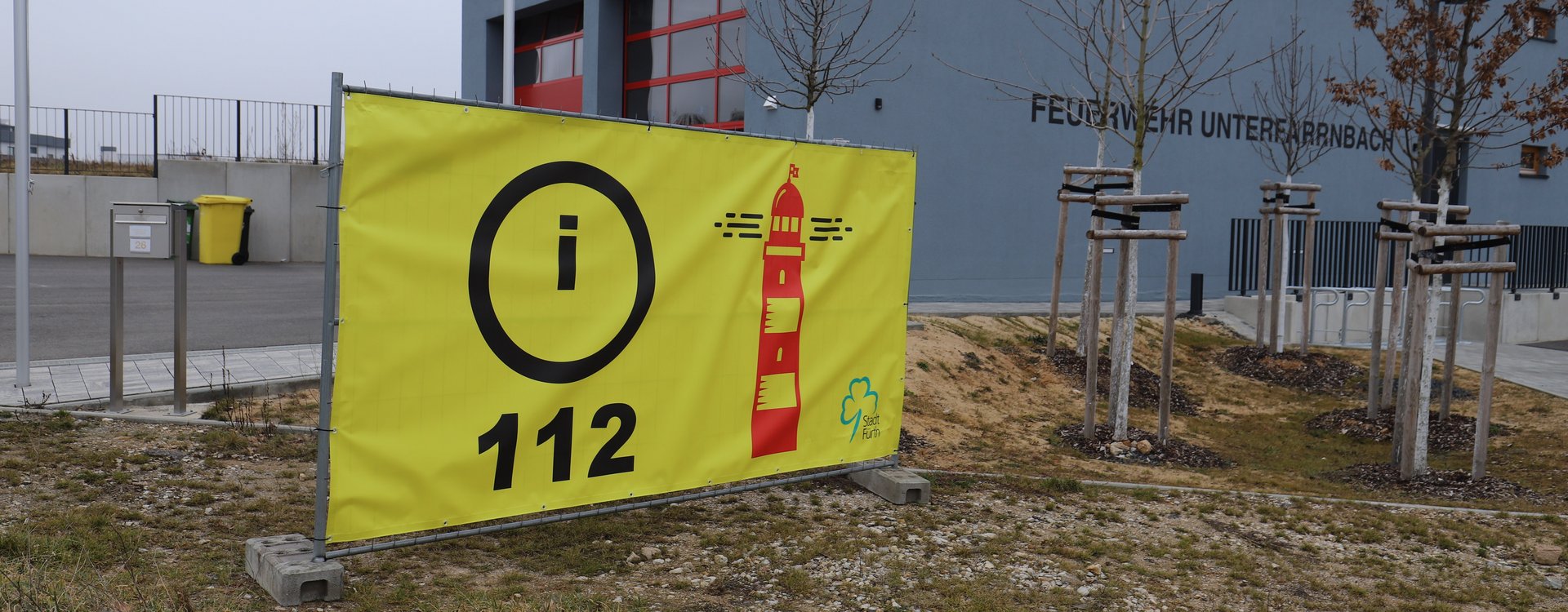 "Leuchttürme" als Anlaufstellen beim Blackout Gelbes Banner mit der Aufschrift "112" und einem Leuchtturm vor dem Feuerwehrgerätehaus Unterfarrnbach.