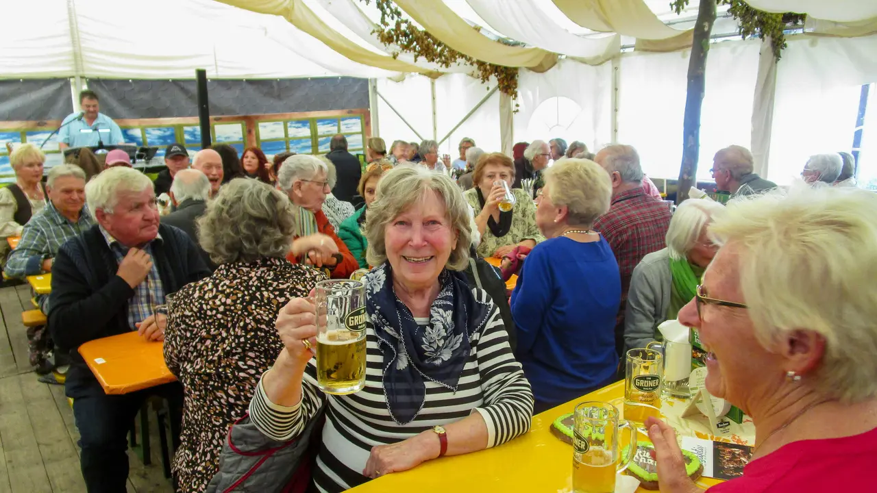 Kirchweihzelt mit älteren Menschen, mittig hebt eine Frau ihr Bierglas zum Prost