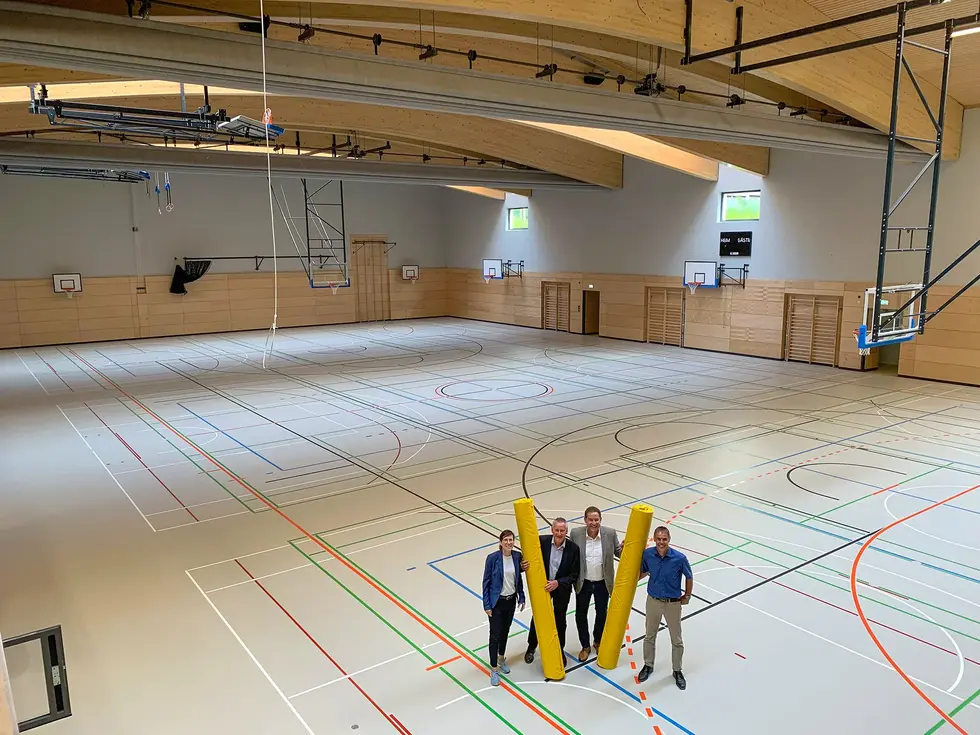 Jung, Lippert, Braun und Stiegler stehen inmitten der neuen, in rund fünf Meter Tiefe eingelassenen Dreifachturnhalle mit gebogenem Gründach.