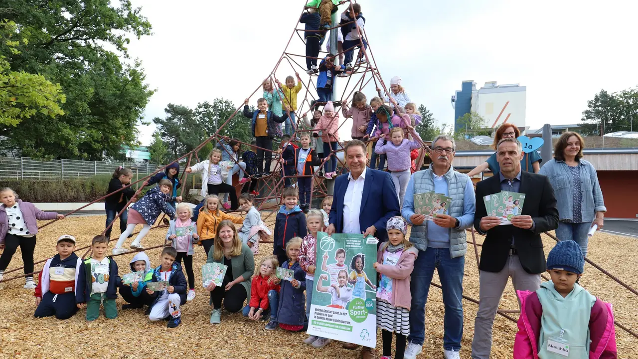 Übergabe der Sportgutscheine Braun und einige Kinder stehen im Pausenhof. Klick öffnet Bild in größerer Ansicht.