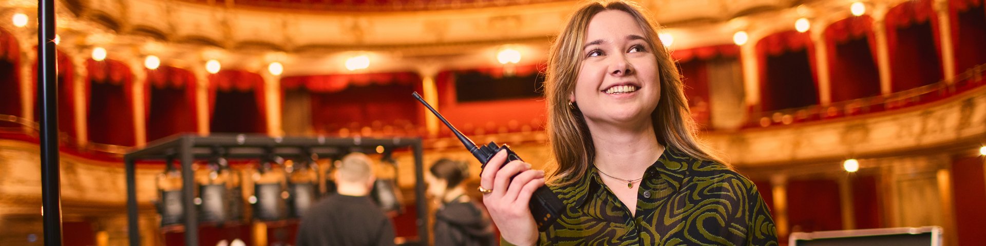Frau mit Walkie-Talkie und Klemmbrett in einem Theater.