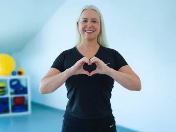 Patricia Hein formt mit den Händen ein Herz vor dem Oberkörper.