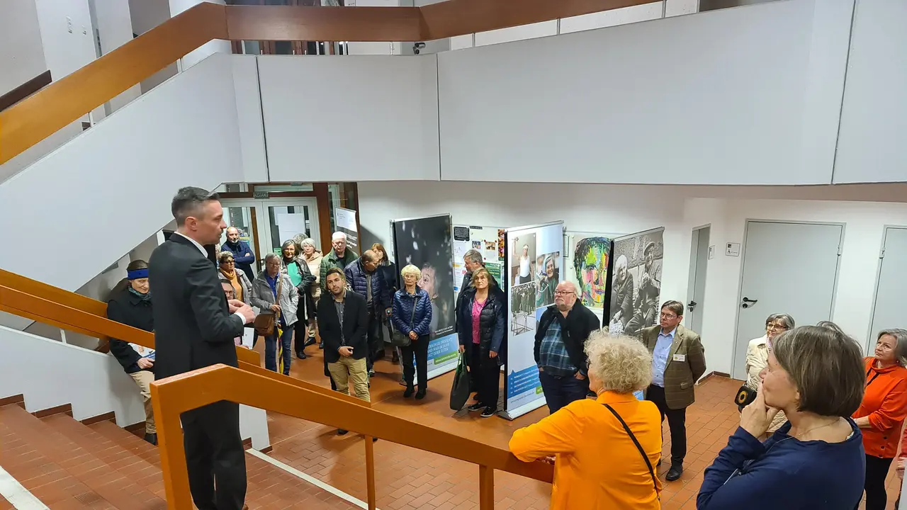 Ältere Besucherinnen und Besucher lauschen den Worten von Kulturreferent Benedikt Döhla bei einer Ausstellungseröffnung