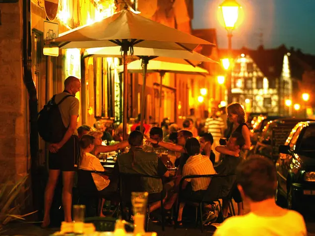 Die Gustavstraße bei Nacht: Im Außenbereich eines Restaurant sind die Tische im Laternenlicht voll besetzt.