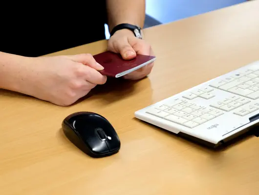 Zwei Hände halten Reisepass an einem PC-Arbeitsplatz. Klick öffnet News in Detailansicht.