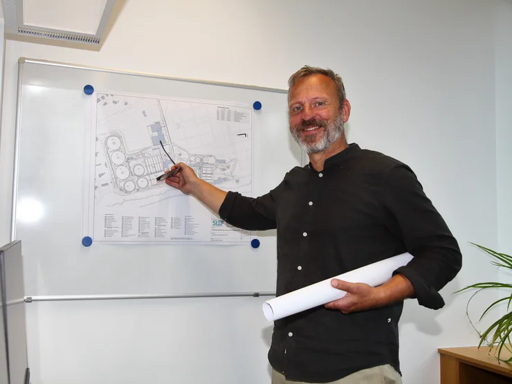 Ein Mitarbeiter, der im Büro vor einem Lageplan steht. 