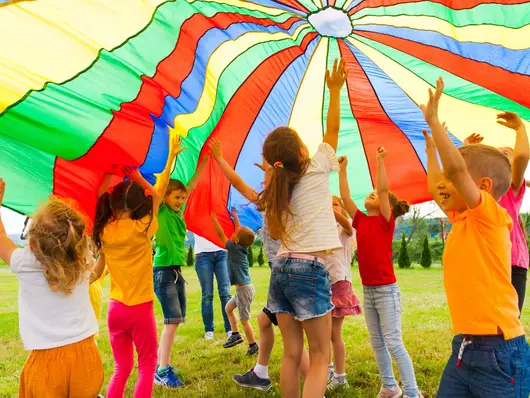 Lachende Kinder halten eine gestreifte Zeltplane in die Höhe