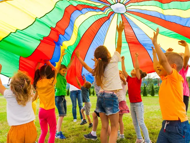 Lachende Kinder halten eine gestreifte Zeltplane in die Höhe