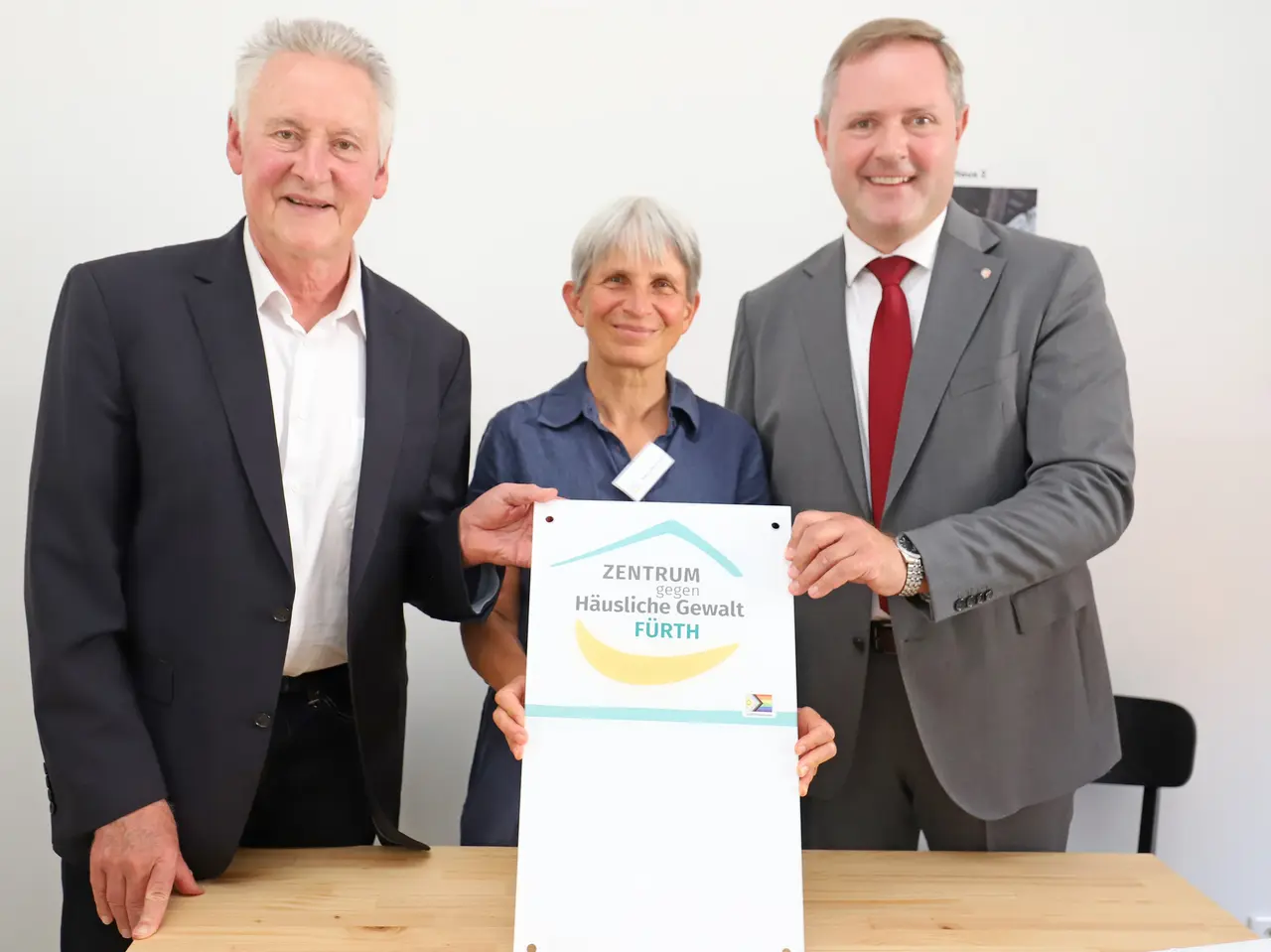 Jung, Vogt-Heeren und Obst halten ein Schild mit dem Logo des Zentrums gegen häusliche Gewalt Fürth.