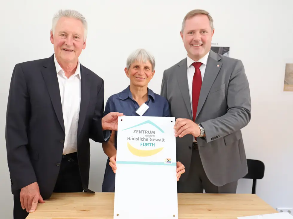 Jung, Vogt-Heeren und Obst halten ein Schild mit dem Logo des Zentrums gegen häusliche Gewalt Fürth. Klick öffnet Bild in größerer Ansicht.