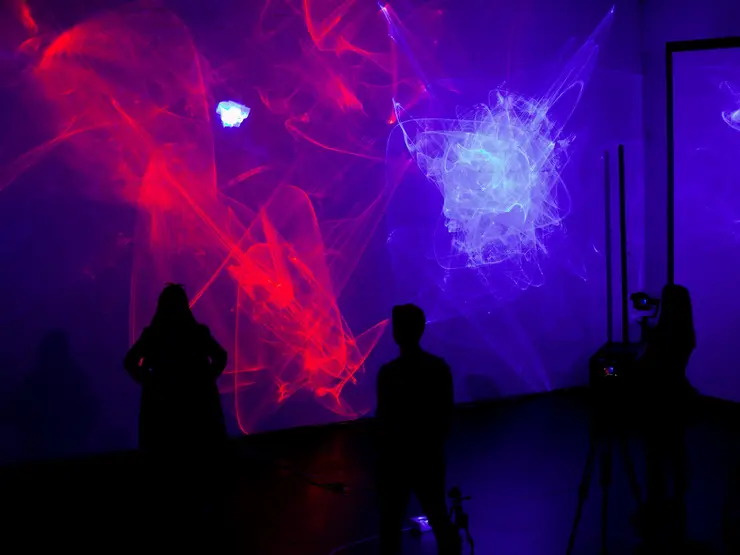 Lichtinstallation mit rot-blauen Lichteffekten auf einer Wand, Menschen beobachten die Projektionen an der Wand.