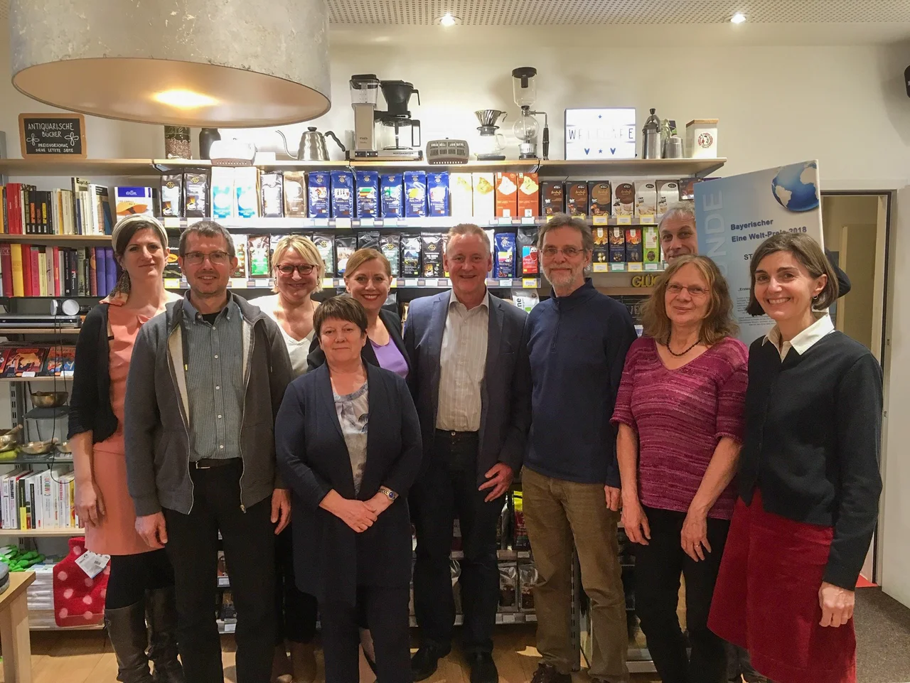 Ob Jung und Steuerungsgruppe vor Regalen im Weltladen. Klick öffnet Bild in größerer Ansicht.