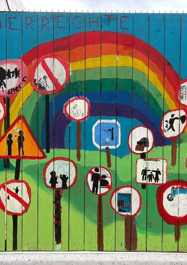 Nahaufnahme bunter Bilder, die am Bauzaun von Kindern erstellt wurden.