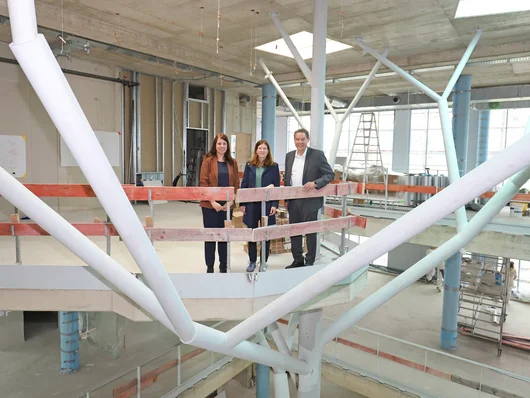 Die Personen blicken auf der Baustelle in die Kamera. Klick öffnet die Meldung.