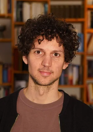 Porträtaufnahme von Lucas Fassnacht vor einem Buchregal.