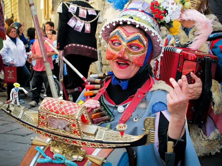 Frau in bunter Maske und Kostüm, spielt eine Trommel und posiert fröhlich auf einer Festveranstaltung.
