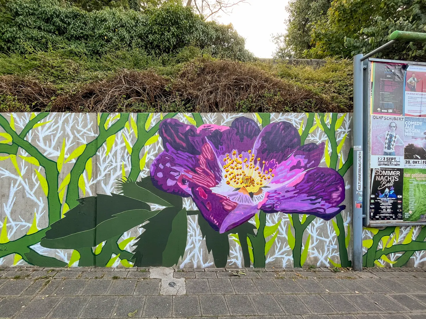 "Um dieser"Rose Willen" ist der Titel des Werkes von Guy Palumbo, das eine violette Rose an einer etwa ein Meter hohen Betonwand zeigt. 