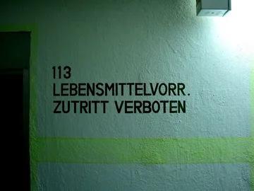 Schwarze Wandbeschriftung mit der Nummer '113' und dem Text 'LEBENSMITTELVORR. ZUTRITT VERBOTEN' auf einer hellen Wand im Kronacher Bunker.