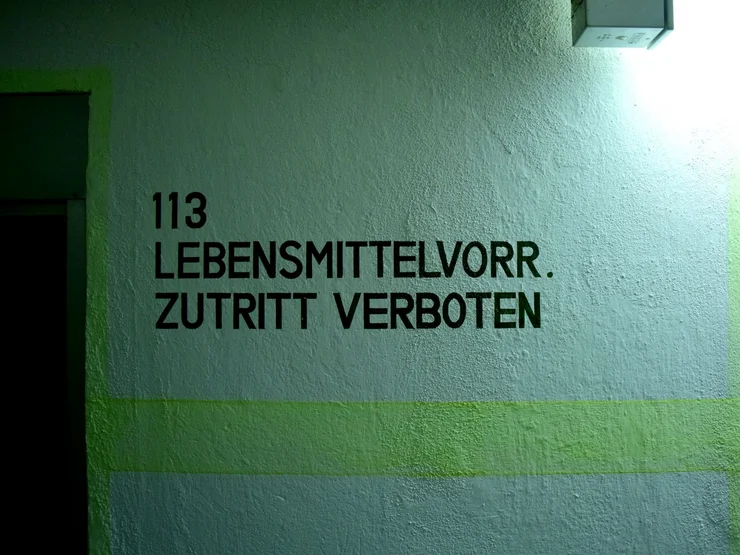 Schwarze Wandbeschriftung mit der Nummer '113' und dem Text 'LEBENSMITTELVORR. ZUTRITT VERBOTEN' auf einer hellen Wand im Kronacher Bunker.