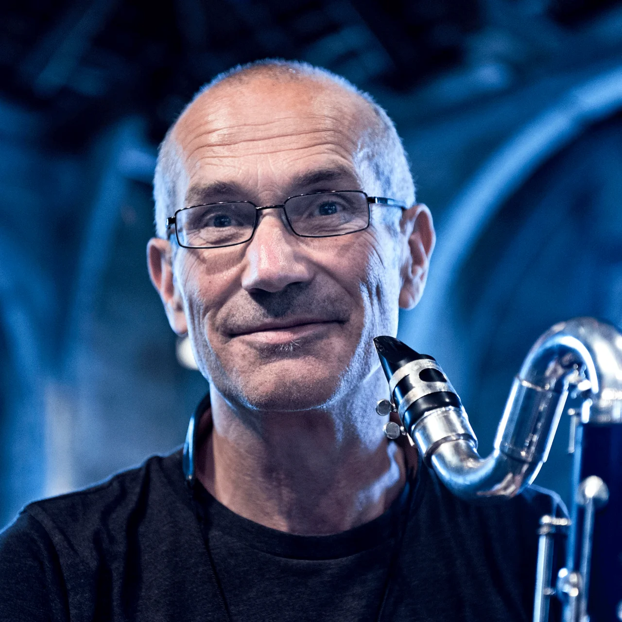 Norbert Nagel mit Saxsophon vor einem unscharfen Hintergrund mit blauem Licht.