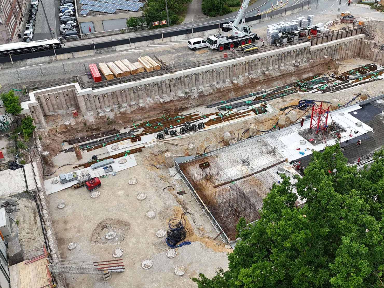Luftaufnahme einer Baustelle mit Fundamenten, Baugerüsten und Baumaterialien, im Vordergrund Bäume