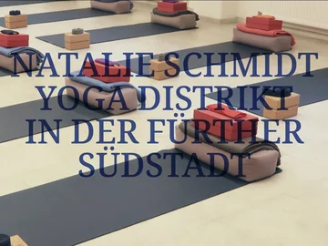 Mehrere Yogamatten mit zusammengefalteten Decken und kleinen Holzkästen in einem hellen Raum mit hohen Fenstern