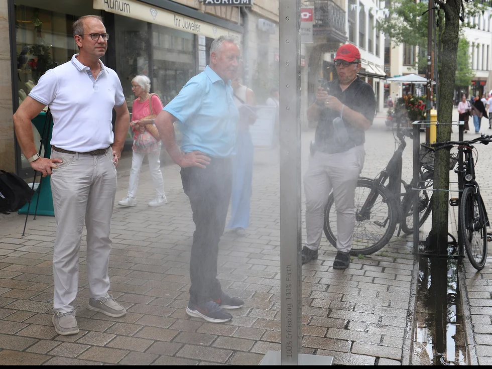 Genannte Personen stehen neben der Säule, die gerade Wassernebel versprüht.
