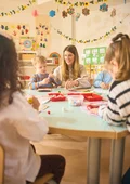 Kinder und Erzieherin sitzen an einem Tisch und basteln gemeinsam.