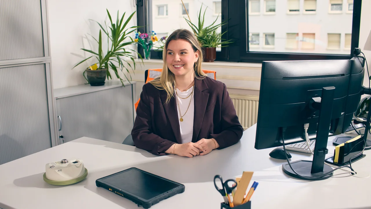 Frau mit Blazer sitzt am Schreibtisch mit Computer und Tablet im Büro.