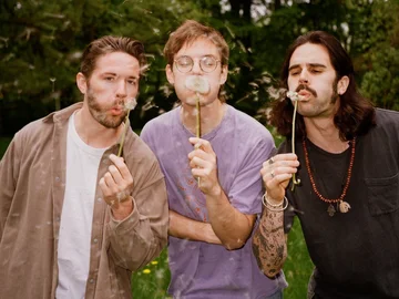 Bandphoto Compadre: 3 junge Männer pusten Pusteblumen