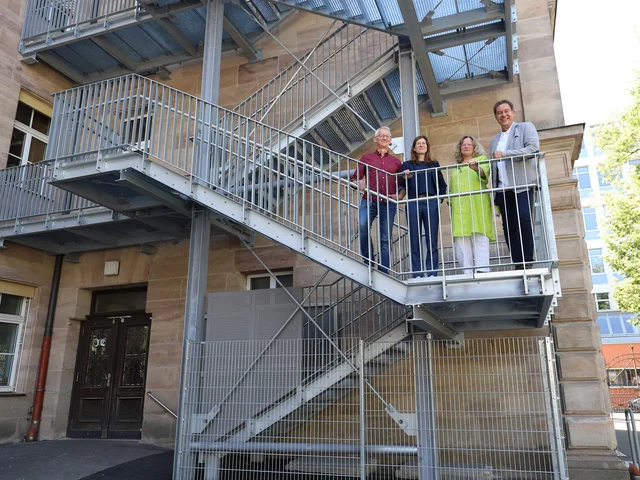 Genannten Personen stehen auf der neuen Brandschutztreppe. Klick öffnet die Meldung.