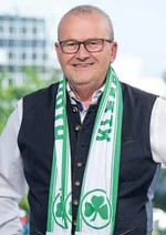 Porträtaufnahme des Stadtrats, der Schal der Spielvereinigung Greuther Fürth trägt, vor einem Fenster