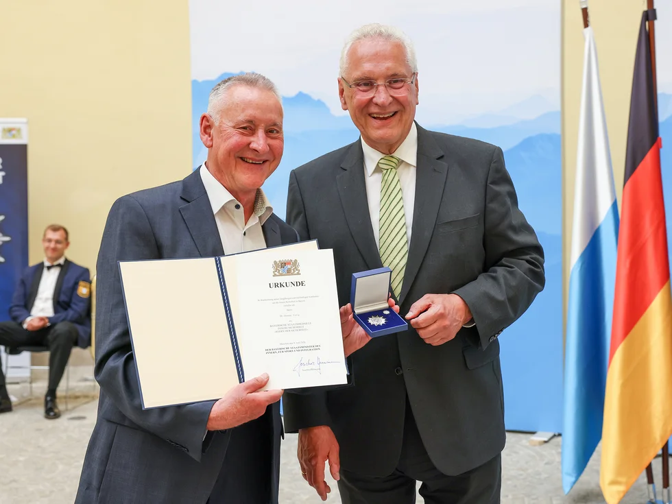 OB Jung hält Urkunde und Stern der Sicherheit als Anstecknadel in einem kleinen Box in der Hand. Neben ihm Innenminister Herrmann.