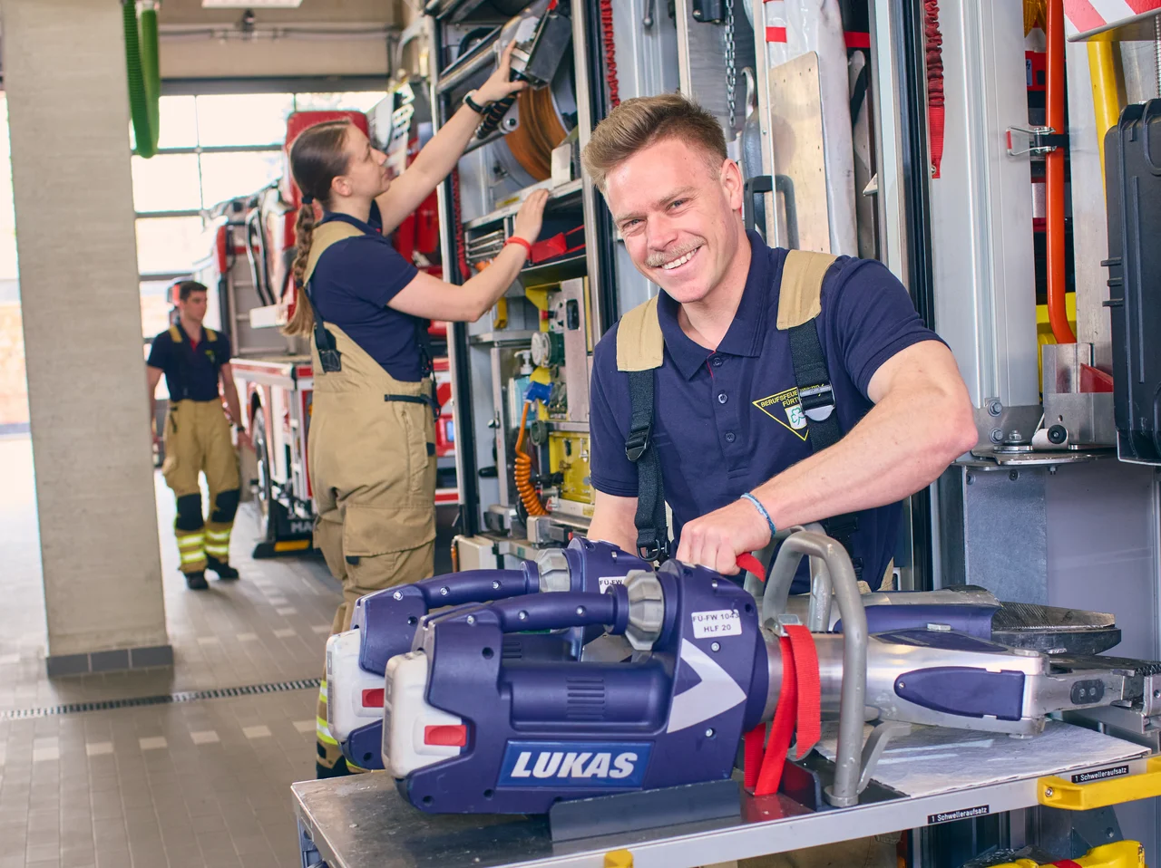 Feuerwehrleute in Uniform entnehmen Ausrüstung aus einem Einsatzfahrzeug in einer Fahrzeughalle.